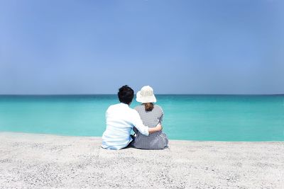 Rear view of friends sitting on shore against sea at beach