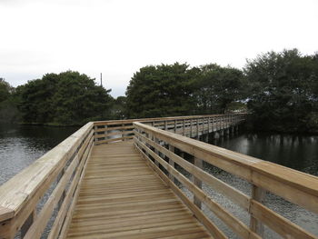 Wooden bridge over lake against sky