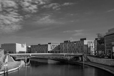 Bridge over river by buildings in city against sky