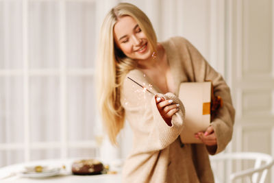Smiling young woman holding mobile phone at home