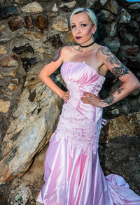 Portrait of woman wearing pink dress while standing by rock