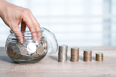 Close-up of hand holding coins in jar on table