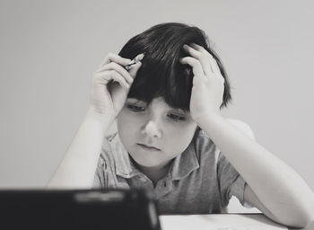 Bored boy with head in hands sitting against wall at home