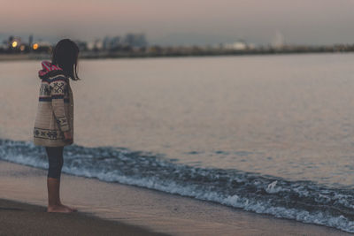 Rear view of woman standing on beach during sunset