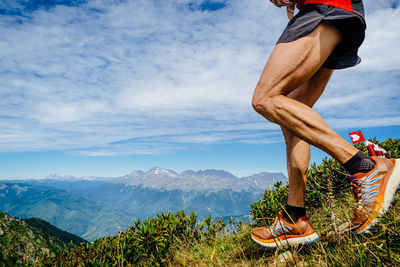 Low section of man standing on mountain against sky