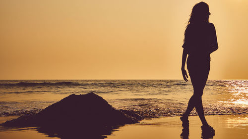 Silhouette woman walking at beach against clear sky during sunset