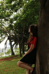Side view of young woman standing by tree