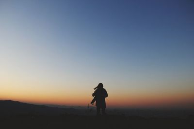 Woman walking on landscape against sky during sunset