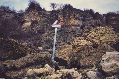 Road sign on rock against sky