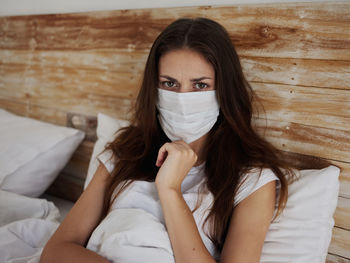 Portrait of woman wearing mask sitting on bed