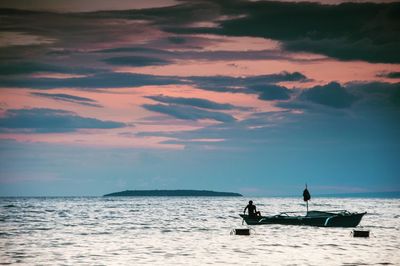 Silhouette man in boat on beach against sky during sunset