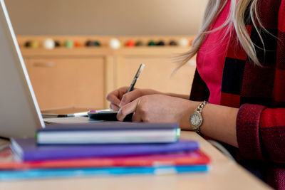 Midsection of woman writing in diary on desk at office