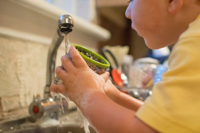 Close-up of boy washing container at kitchen sink