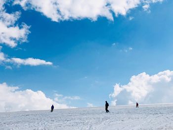 People on snowy land against sky during winter