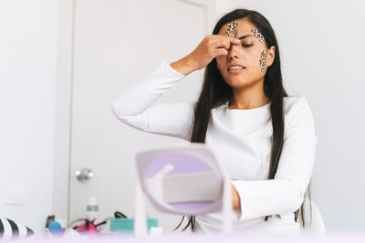 Young brunette woman with long hair cosmetologist makes face taping looks in the mirror in office