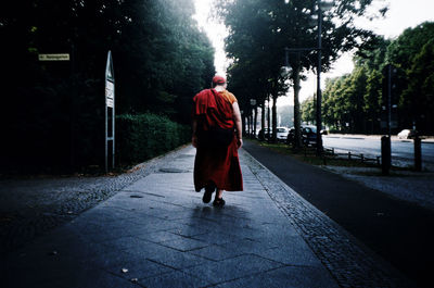 Full length rear view of monk walking at sidewalk in city