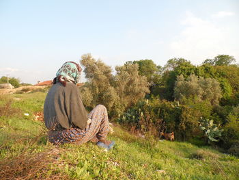 Rear view of man sitting on field against sky