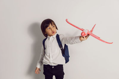 Boy child in a white shirt and jeans flies on a red airplane toy at the white wall of the house