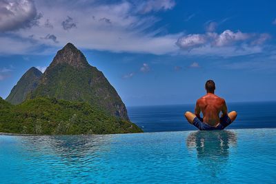 Rear view of shirtless man relaxing by infinity pool against sea