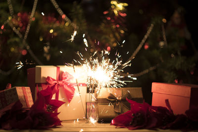 Close-up of lit sparklers by christmas presents at night