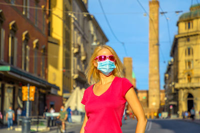 Woman wearing sunglasses standing against buildings in city