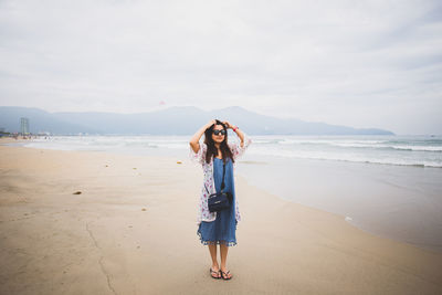 Woman standing with hands in hair at my khe beach against sky