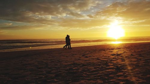 Silhouette woman on beach against sky during sunset