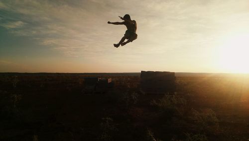 Silhouette man jumping on field against sky during sunset