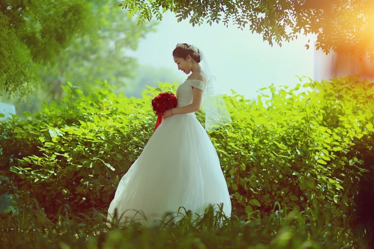 wedding, bride, wedding dress, life events, love, bridegroom, women, young women, celebration, groom, young adult, celebration event, wedding ceremony, standing, married, wife, real people, nature, bouquet, togetherness, outdoors, well-dressed, grass, day, beauty in nature, full length, flower, beautiful woman, tree, people