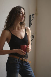 Young woman looking away while standing against wall