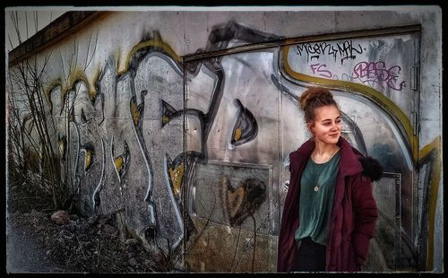 Young woman standing against graffiti wall