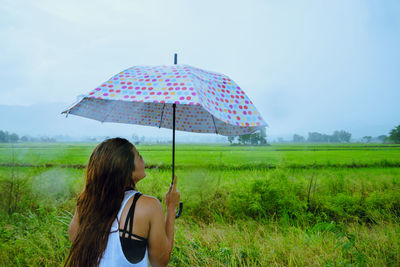 Woman with umbrella standing on field against sky