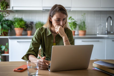 Pensive woman freelancer working at home, reading text document from laptop screen attentively