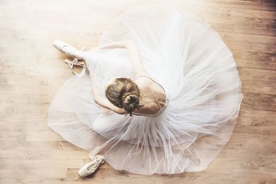 High angle view of ballerina sitting on hardwood floor