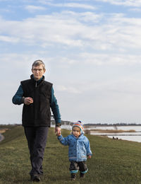 Full length of grandfather and granddaughter walking on field against sky