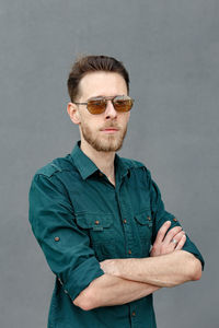 Portrait of young man wearing sunglasses while standing against wall