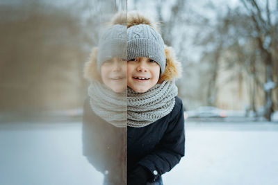 Winter portrait of cute caucasian boy of elementary age in knit hat with pompom in city