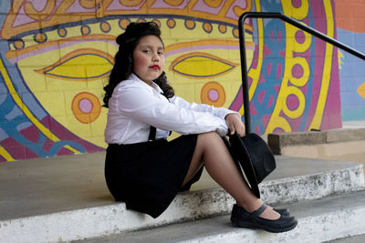 Full length of woman sitting against graffiti wall