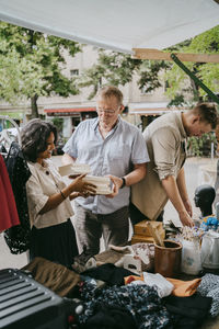 Senior male owner assisting female customer buying books at flea market