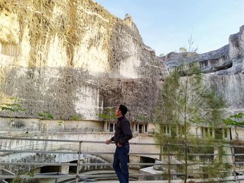 Rear view of man standing on rock against sky