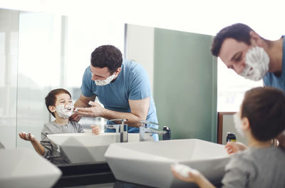 Father applying shaving cream on son face