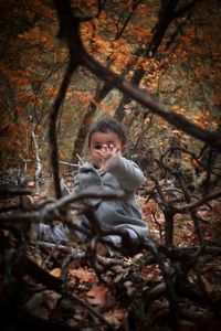 Cute girl gesturing while sitting in forest during autumn