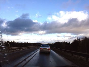 Cars on road against cloudy sky