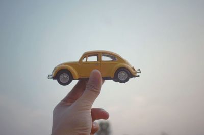 Cropped hand holding toy car against clear sky