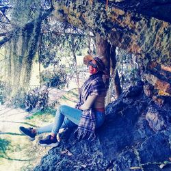 Woman sitting on rock against trees