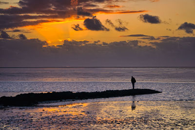Silhouette person on beach against sky during sunset