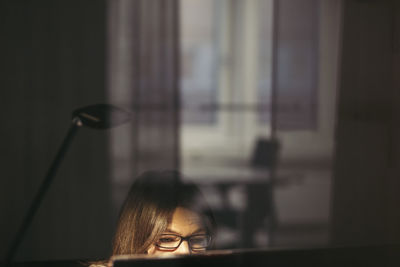 Businesswoman wearing eyeglasses using computer seen through glass at office