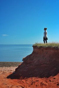 Woman standing on cliff at beach against blue sky