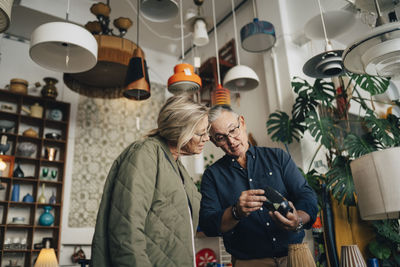 Low angle view of senior male owner reading price tag of vase for female customer at store