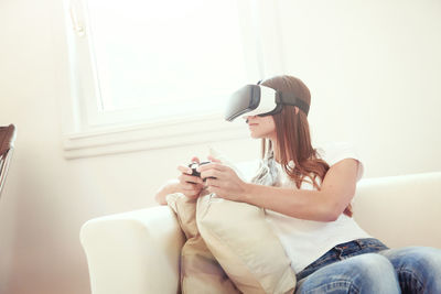 Young woman using phone while sitting on sofa at home